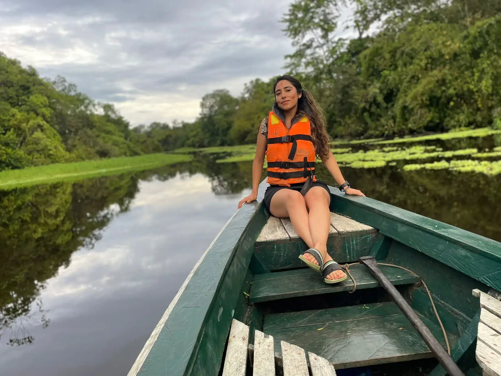 Visitante sentada en una canoa de madera verde sobre una cocha de aguas quietas