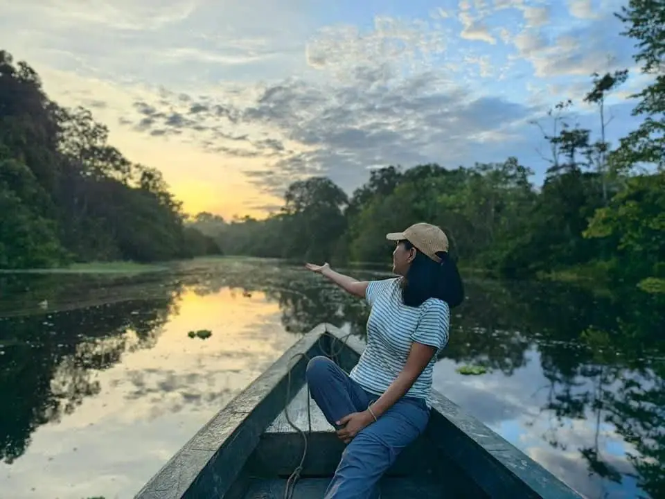 Visitante sentada en la proa de una canoa mientras cae el sol sobre el río